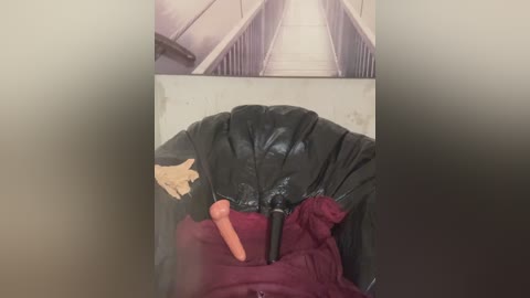 A video captures a black garbage bag with a penis-shaped object inside, set against a dull, industrial background featuring metal railings and a cylindrical structure.