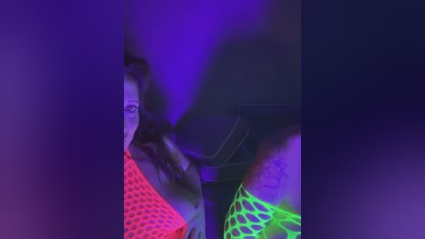 Video of a woman in a bright, neon green fishnet top, with purple and red lighting creating a trippy, psychedelic effect. Her face is partially obscured by her dark hair.