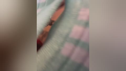 The image is a blurred video featuring a close-up of a person's hand and a portion of a checkered cloth with pastel pink and green squares. The focus is unclear, making it difficult to discern specific details.