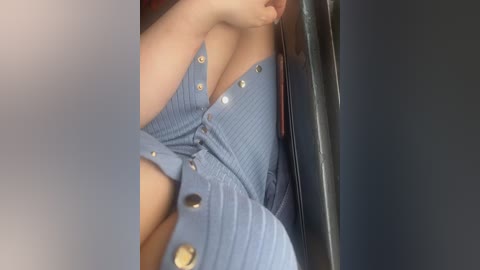 Video of a woman's upper torso in a blue, ribbed, button-up dress with a plunging neckline, revealing ample cleavage. She is seated in a car, with a dark, leather interior. Her skin is fair, and her lips are slightly parted, showing a hint of teeth.