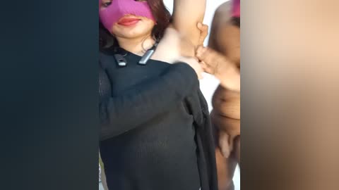 Media: A close-up video of a woman with light skin, wearing a black dress and pink mask, exposing her underarm. Another person's hand is visible on her right side, suggesting a close interaction.