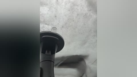 Black-and-white video of a large, cylindrical air conditioning unit mounted on a textured, rough concrete wall. The unit's fan blades are visible, and the background is blurred, creating a sense of depth.