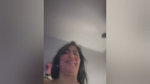 A blurred video shows a woman with long black hair, wearing headphones, laughing. She is in a white room with a ceiling light.