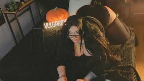 Video of a Halloween-themed bedroom with a woman in black lingerie and a pumpkin on a bed, wearing glasses and a \"MILF\" headband.