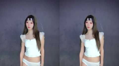 Video of an Asian woman with long brown hair, wearing a white lace top and matching panties, standing against a gray backdrop, with a slight left-right mirror effect.