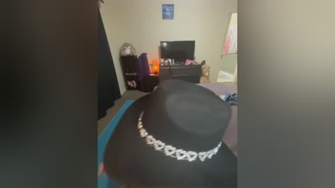 Video of a cluttered bedroom with a black hat, a bed, a desk, and a TV, featuring a cozy, warm ambiance.