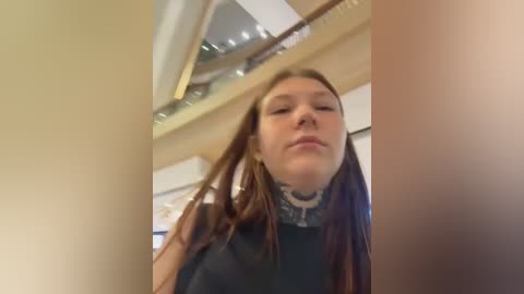 Video of a Caucasian woman with long brown hair, wearing a black shirt, adjusting her hair in a room with beige walls and a ceiling fan.