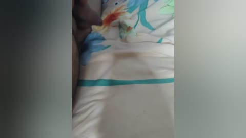 A video captures a person lying on a bed with a white sheet featuring vibrant blue and green floral patterns. The individual's skin tone is dark, and the bedding is slightly wrinkled.
