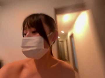 A blurry video of a topless Asian woman with short dark hair and a white face mask, taken indoors with a warm, dim light.