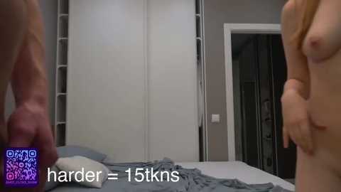 Video of a nude man and woman in a modern bedroom, with a white sliding door closet in the background, showing the man's erect penis.