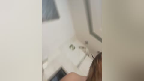 A close-up video of a person's hand holding a white, rectangular object with a green button, partially obscured by blurred background elements.