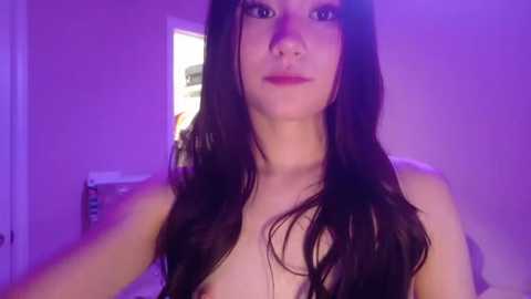 Video of a young woman with long, dark hair, light skin, and small breasts, standing indoors, bathed in purple lighting, wearing nothing.