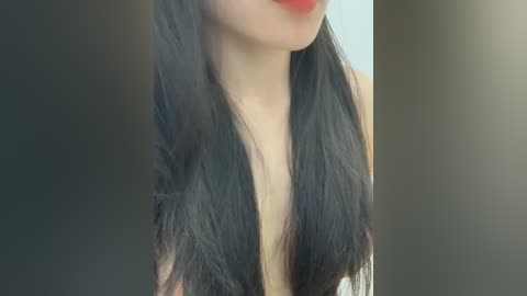Video of a woman with long, straight black hair and pale skin, wearing a deep V-neck top, with a blurred background.