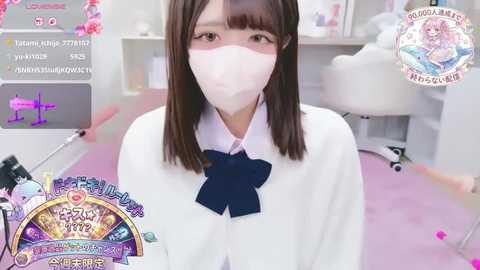 A video of a young Asian woman with straight brown hair, wearing a white mask, a white blouse with a navy blue bow, and a pink background.