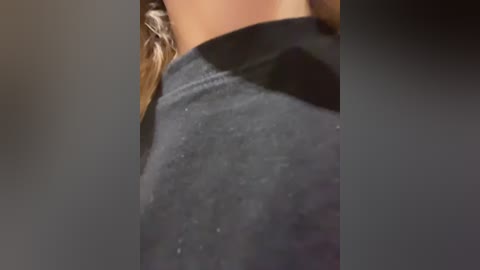 Close-up video of a person's upper back, showing a dark grey T-shirt with subtle texture, highlighting the fabric's softness. The background is blurred, emphasizing the subject.