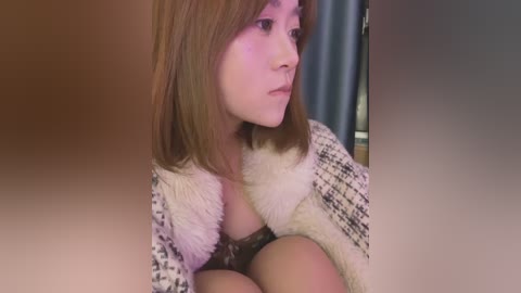 Media: A close-up video of a young Asian woman with shoulder-length brown hair, wearing a white fur-trimmed coat, sitting indoors with blurred background.