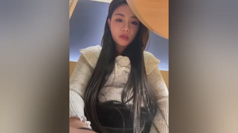 Media: Video of an East Asian woman with long black hair, wearing a white ribbed sweater with a black leather handbag, against a blurred background.