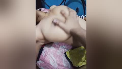 A video of a person's bare chest, with visible nipples and a hand gently squeezing a breast. The background features a blue wall and a yellow blanket.