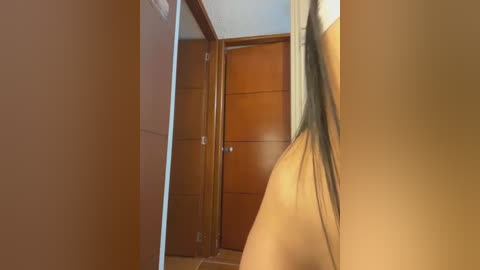 Video of a partially visible, naked person with light skin, long black hair, and a slender physique, standing in a wooden doorframe, viewed from behind, emphasizing the buttocks.