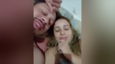 A video captures a close-up of a man and woman in bed, both with closed eyes, smiling, and touching each other's faces.