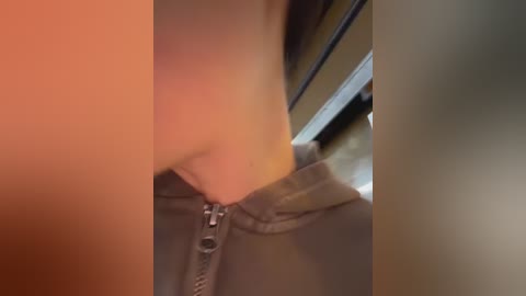 Video of a person's lower body, showing a partially unzipped gray zipper on a pair of pants. The background features a blurred, beige wall and a window with light streaming in.