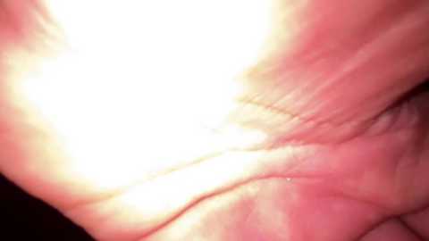 Close-up video of a person's hand, with a bright, white light shining directly onto the skin, causing a glare and blinding effect. The background is dark and indistinct, focusing on the illuminated hand.