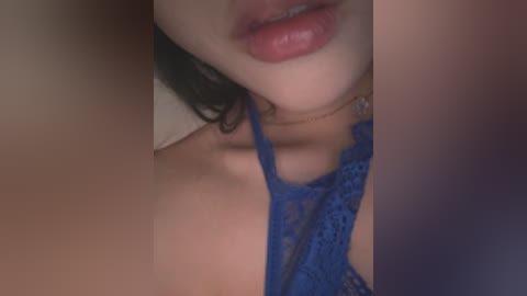 A close-up video of a woman with fair skin and full lips, wearing a blue lace bralette, partially visible. The background is blurred, with a soft focus.