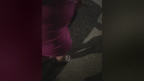 Media: A video captures a person wearing a tight, magenta dress with a high waist, walking on a dimly lit street. The image is grainy and slightly blurred, focusing on the lower half of the person.