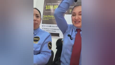 Video of two female security guards in blue uniforms with badges, one raising her arm, smiling, and the other standing beside her. Background shows a promotion poster for a loan.