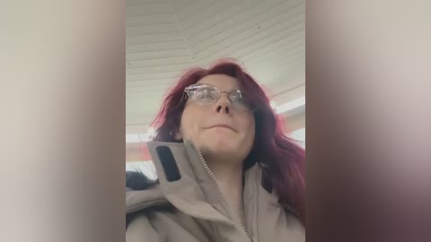 Media: A video of a woman with red hair, wearing glasses and a beige jacket, taken from a low angle, creating a dramatic perspective.