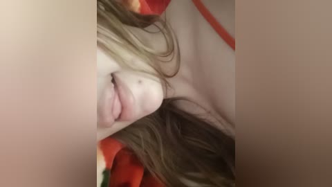 A close-up video of a young woman with light skin, brown hair, and full lips. She wears a red and green striped shirt, partially visible. The background is out of focus.