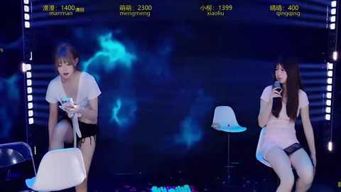 Video of two women in white dresses, seated on chairs in a dimly lit room with blue lighting and smoke effects.