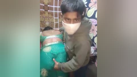 A video shows a man in a green hoodie forcibly dragging a woman in a green sari, with her back exposed, in a dimly lit room with floral wallpaper.