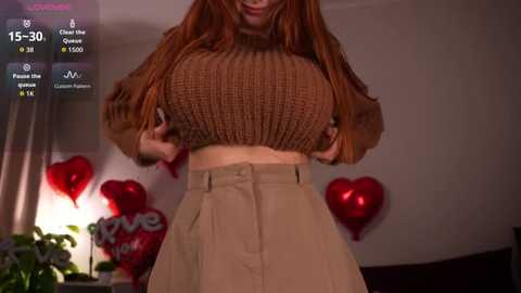 Video of a woman with long, reddish-brown hair, wearing a brown ribbed sweater and high-waisted beige skirt, holding her sweater open, surrounded by red balloons, and a \"Love You\" sign in a dimly-lit room.