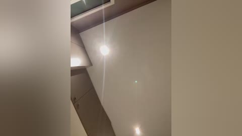 Video of a modern, beige-painted ceiling with a recessed light fixture emitting a soft, warm glow. The ceiling is angled and slightly sloped, creating a contemporary architectural design.