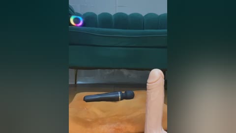 A video showing a large, realistic, tan-colored dildo lying on a wooden floor, next to a green velvet couch with a rainbow light ring hovering above it.