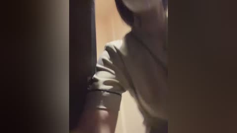 Video of a person, possibly a man, with a light complexion, wearing a light-colored shirt, leaning into a doorway. The background is blurred and dimly lit, suggesting an indoor setting.