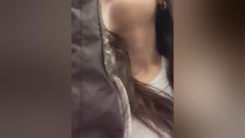 A blurred, close-up video of a person's face and upper torso, partially obscured by a black jacket, suggesting a casual, indoor setting.