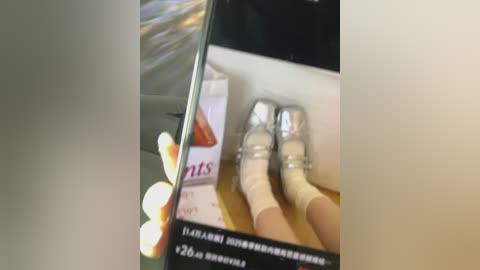 A video shows a person's hand holding a smartphone displaying a product page with a box of cigarettes and a pair of silver high-heeled shoes.
