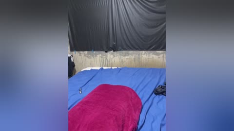 Media: Video of a simple outdoor campsite featuring a blue tarp roof, a red sleeping bag, and a blue sleeping mat. The background shows a worn concrete wall.