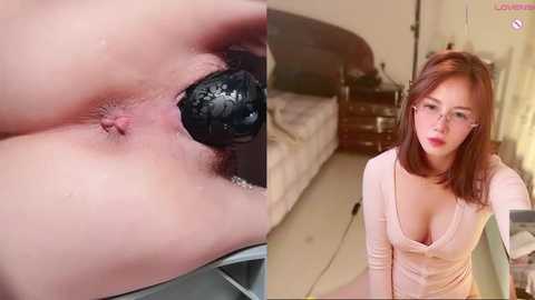 Video of a woman with fair skin, short red hair, and glasses, wearing a low-cut pink top, standing in a bedroom with a bed and nightstand. Close-up of a black, textured object inserted into her anus.