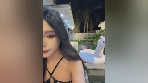 Media: Video of a young Asian woman with long black hair, wearing a black strappy top, standing in a modern outdoor setting at night.