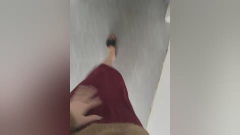 Video of a person in a red shirt and brown pants standing on a white surface, with a blurred background of a light-colored room.