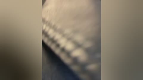 A blurred video of a person's hand holding a fabric item, possibly a sweater, with a textured surface. The background is a plain, light-colored wall. The image has a soft focus, making details indistinct.