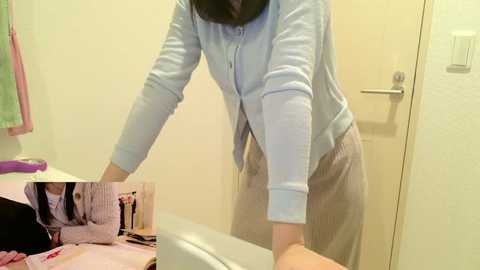 A video shows a person in a light blue sweater and striped pants, bending over a bathtub, with a magazine open on the tub's edge. The background includes a towel rack and a pink towel.