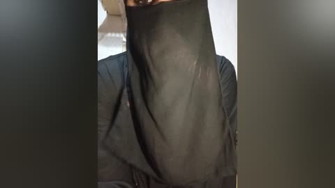 Media: A video of a person wearing a black niqab covering their face, with a hint of brown skin visible at the edges. The background is blurred and neutral-colored.