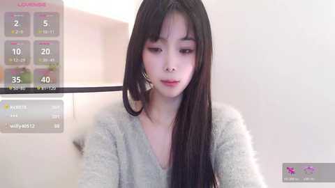 A video of a young Asian woman with long black hair, fair skin, and a V-neck grey sweater, set against a white background. A virtual reality interface overlaid with weather and time details is visible.