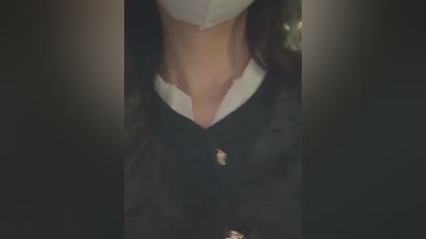 Video of a person's upper torso in a black, buttoned-up blazer over a white collared shirt, with blurred background, focusing on the neck and shoulders.