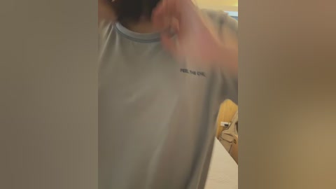 Media: Video of a person adjusting a light blue, short-sleeved athletic shirt with \"Reebok\" logo. The background shows blurred indoor elements with warm lighting.