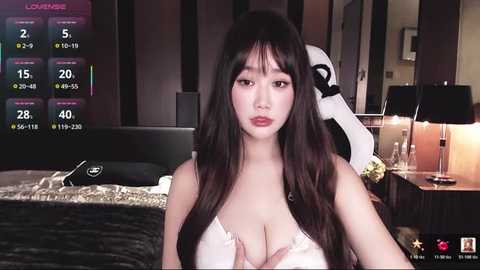 Video of an Asian woman with long, straight black hair, wearing a white lace bra, standing in a modern bedroom with a digital clock displaying 5:00 AM, a black bed, and a white robot.